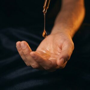 Kapka zlatavého pečujícího oleje stékající z pipety do dlaně pro vědomou masáž a uvolnění.